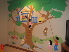 a child's room with a tree painted on the wall and children playing in it