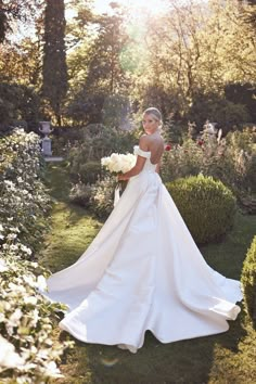 a woman in a white wedding dress is standing in the middle of some bushes and flowers