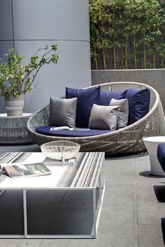 an outdoor seating area with blue cushions and pillows on the couches, coffee table and potted plant