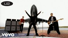 two men are playing guitars in front of an airplane and another man is holding his arms up