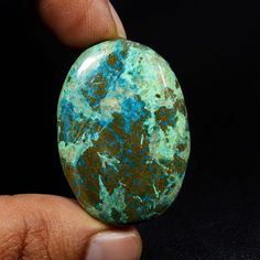 a person holding an oval shaped turquoise and brown stone in their left hand, on a black background