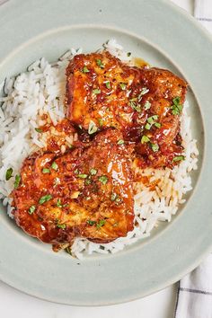 two pieces of meat with sauce on top of rice in a blue and white plate