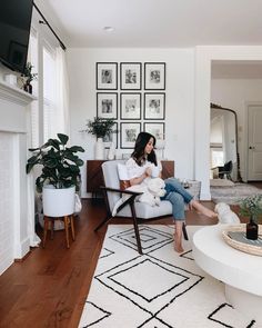 a woman sitting on a chair in a living room with a fireplace and pictures on the wall