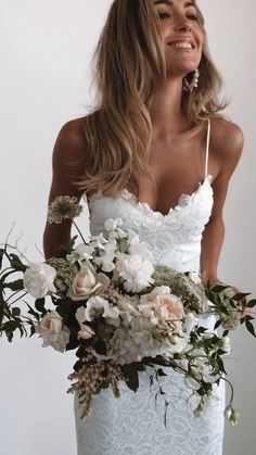 a woman wearing a white dress holding a bouquet of flowers in her hand and smiling