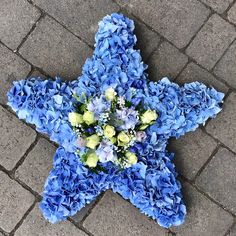 a star shaped arrangement of blue hydrangeas and yellow roses sits on the ground