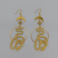 ♡ Cosmic Snake Hoops Dangle Earrings ♡ ♡ Our gold celestial slithering serpent earrings make perfect gifts to delight yourself or those you love! The large snake and hoops at center surrounded by the sun and stars evoke feelings of peace and eternal beauty, especially when kissed by the light. A gorgeous ear hook pair of earrings that shines through and accentuates the beauty of every outfit. Handmade with quality brass stainless steel alloy ♡ C O S M I C ∙ S N A K E ∙ E A R R I N G S ▂▂▂▂▂▂▂▂▂▂ Handmade Gold Snake Earrings, Handmade Gold Snake-shaped Earrings, Celestial Metal Dangle Hoop Earrings, Celestial Style Metal Dangle Hoop Earrings, Gold Snake Jewelry For Pierced Ears, Gold Snake-shaped Jewelry With Pierced Ears, Gold Snake-shaped Earrings With Pierced Ears, Gold Snake Earrings For Party, Trendy Snake-shaped Metal Jewelry