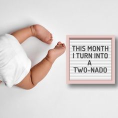 a baby laying on its back next to a sign that says, this month i turn into a two - nado