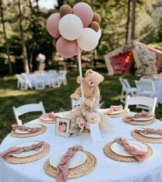 a teddy bear sitting on top of a table with plates and place settings in front of it