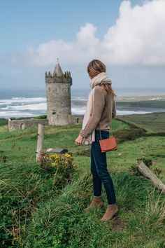 a woman standing on top of a lush green hillside next to a tall tower building