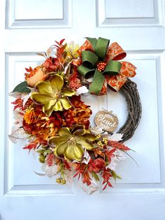 a wreath is hanging on the front door with autumn leaves and flowers around it,