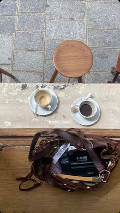 two cups of coffee sit on a table next to an open purse and a cup of espresso