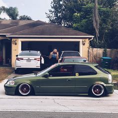 a green car parked in front of a house next to a woman taking a photo