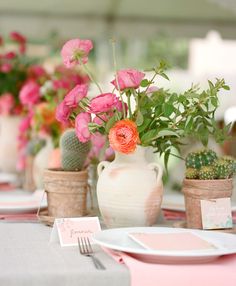 pink flowers are in vases next to white plates and utensils on a table