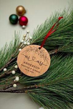 a wooden ornament hanging from a pine tree with ornaments around it and the words mr and mrs on it