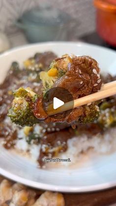 a white plate topped with meat and broccoli covered in gravy next to chopsticks