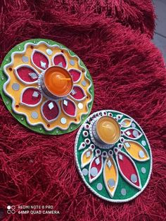 two decorative items sitting on top of a red carpet next to each other and one has an orange candle in the center