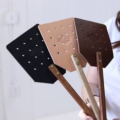 a woman holding up four pieces of leather with holes in them and wooden sticks sticking out of the sides