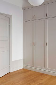 an empty room with white cupboards and wood flooring in front of the door