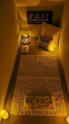 a bed with pillows and candles on the floor in a room that is lit up