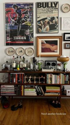 a book shelf filled with lots of books on top of a hard wood floor next to a wall covered in posters