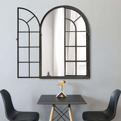 two chairs and a table with a vase on it in front of an arched mirror