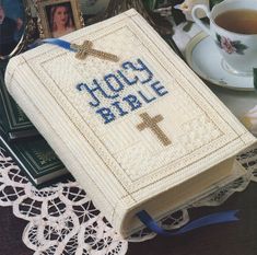 a cross stitched book sitting on top of a table next to a cup and saucer