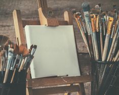 an easel full of paint brushes and other art supplies on a wooden background with copy space