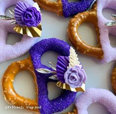 purple and gold decorated pretzels with flowers on them are arranged in the shape of hearts