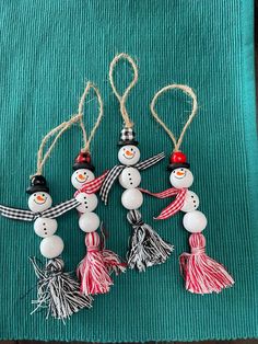 four snowman ornaments hanging from string on a green cloth with red and white tassels