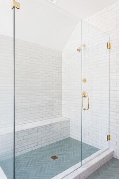 a walk in shower sitting next to a white tiled wall and floor with gold fixtures