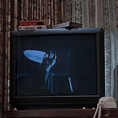 a television sitting on top of a wooden shelf in front of a curtained wall