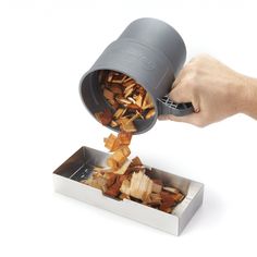 a person is pouring something out of a can into a tin with wood chips in it