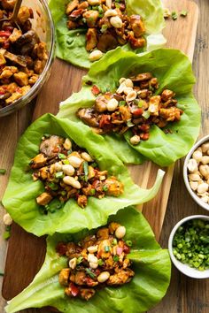 lettuce wraps filled with chicken and vegetables on a cutting board next to bowls of beans