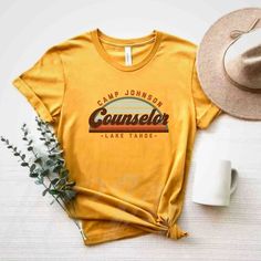 a t - shirt that says camp bachelor on it next to a hat and flowers