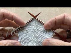 two hands holding knitting needles over a knitted object