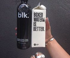 a person holding up a bottle and a carton that says boxed water is better