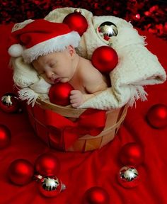 a baby wearing a santa hat in a basket surrounded by christmas balls and baubs