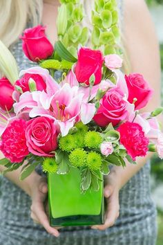 a woman holding a green vase filled with pink flowers