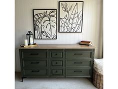 two paintings hang on the wall above a green dresser with drawers and books in front of it