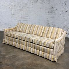 a striped couch sitting on top of a cement floor next to a white brick wall