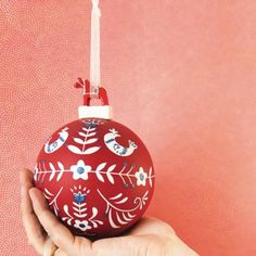 a hand holding an ornament in front of a pink wall with red and white designs