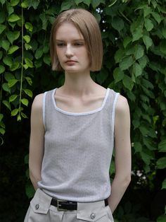 a young woman is standing in front of some trees wearing a gray shirt and khaki pants