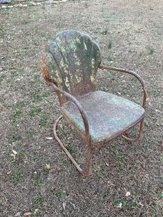 an old rusty chair sitting in the middle of a grass covered field with dirt on it