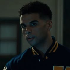 a young man in a black and yellow jacket looking at the camera while wearing earrings