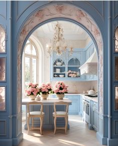 an archway leading into a kitchen with blue cabinets and pink flowers on the table in front of it