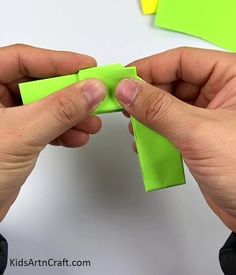 two hands are holding green sticky notes on a white surface and one hand is pulling them out