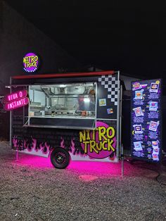 a food truck parked in front of a building with neon signs on it's side