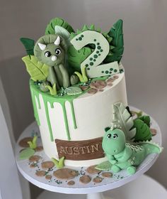 a two tiered cake decorated with green and white icing, featuring dinosaurs sitting on top of it