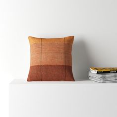 an orange pillow sitting on top of a white shelf next to a stack of books