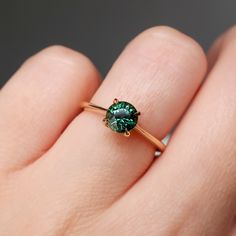 a person's hand holding a ring with a green stone on it and gold band